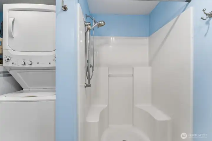 Stackable washer/dryer and walk-in shower in bathroom.