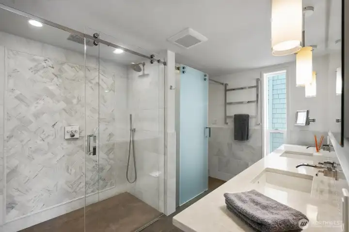The primary bath offers custom tile shower with Hansgrohe shower fixtures with ceiling, wall and handheld shower heads and custom water wicking glass. Dual laCeva sinks, quartz countertops and pendant lighting.