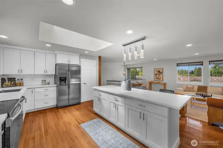 Stunning view from the kitchen looking into the living room, highlighting the abundant natural light from the expansive skylights and the gleaming hardwood flooring throughout.