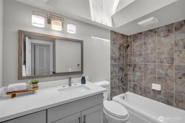 Pristine upper-level main bathroom featuring a sleek gray vanity and classic stone tile work
