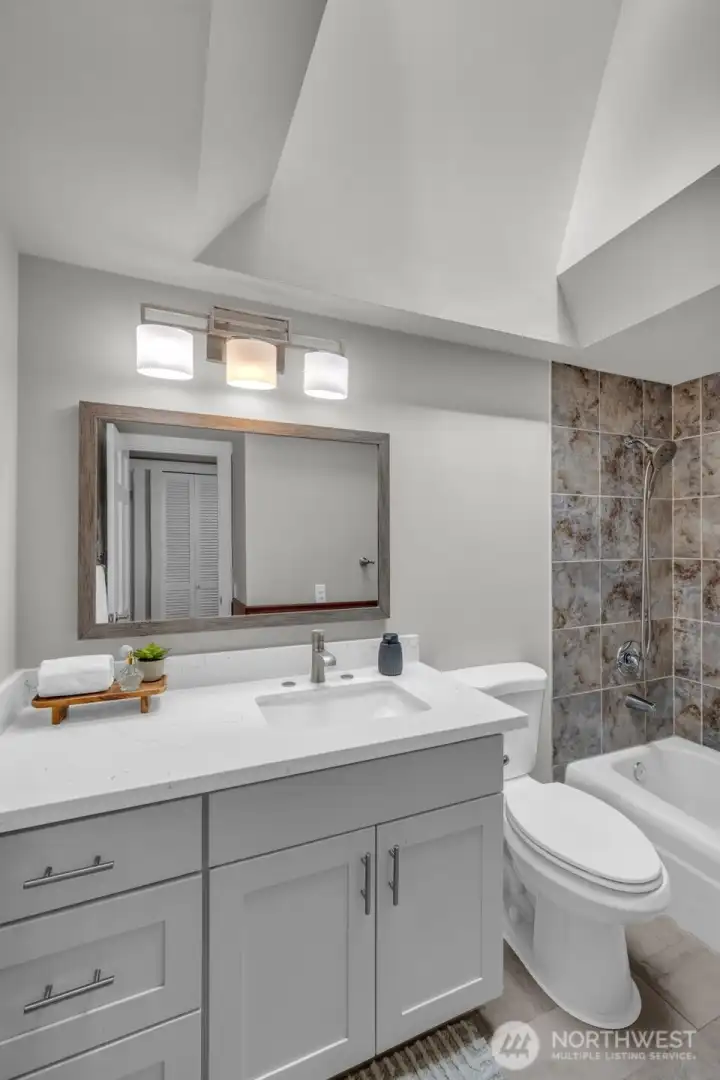 Upper-level main bathroom featuring a sleek gray vanity and classic stone tile work