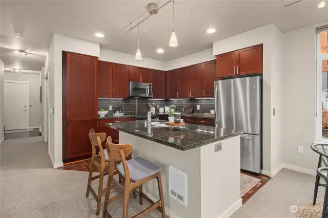 Open concept kitchen has an eat-in bar, granite counter tops, cherry cabinets and modern stainless appliances.