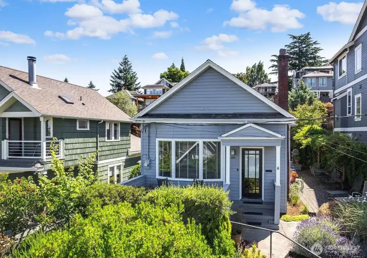 Light, bright & above it all this 1906 Craftsman features a light-filled open concept tastefully updated to contemporary standards. 3 bedrooms & 2 baths on a lushly landscaped lot with an unobstructed view from a wall of western windows to the Olympics & partial Elliott Bay views. Gorgeous hardwood floors throughout complement the period detail of mantled fireplace & built-in bookcases typical of this vintage. The thoughtful 3 point plan of range-frig-sink will save steps.There is ample prep, cupboard & cabinet space here to please the chef. The primary bedroom & bath sits quietly at the back of the house looking out over the gardens, with two more guest bedrooms serving as office or daybed. One car garage too. Here you'll enjoy outdoor living all summer long!