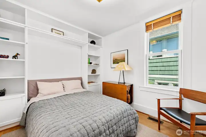 The guest bedroom features a Murphy bed with built-in bookshelves. This is a large & comfortable bedroom with room for a nightstand and a sitting / reading area.