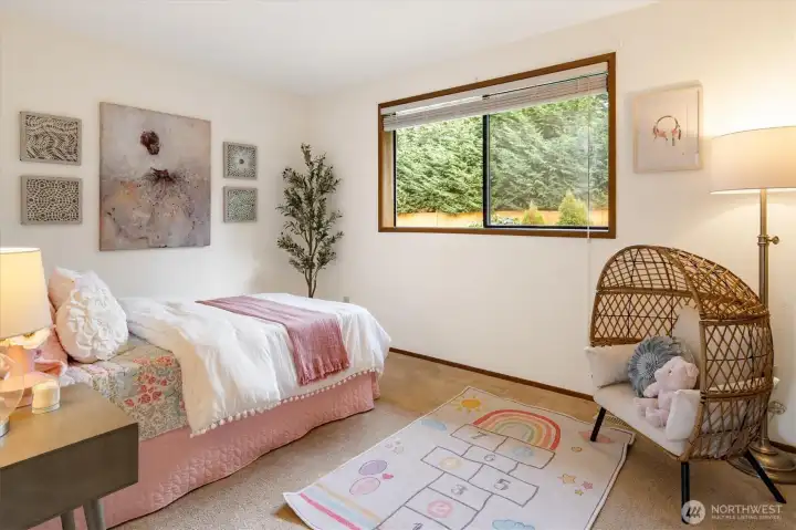 A well-sized bedroom with a wide window overlooking greenery offering a calm and practical space for rest or work.