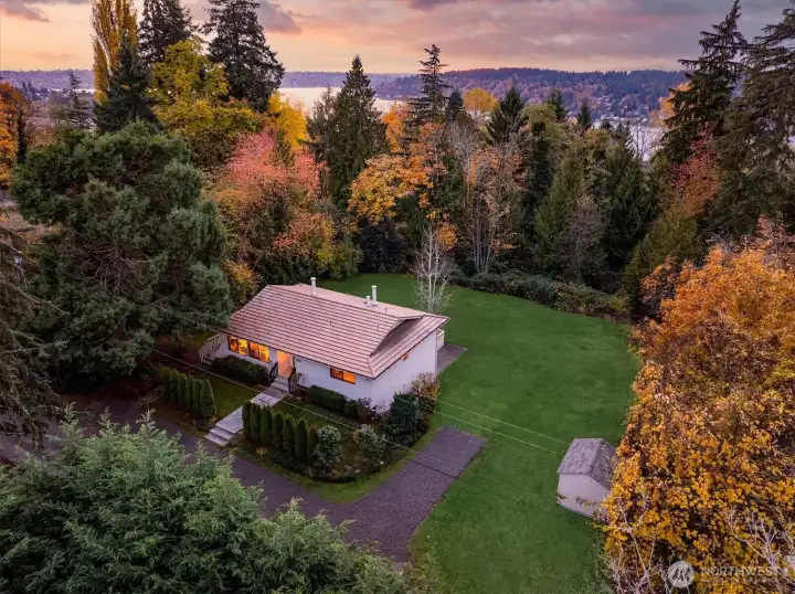 At dusk the home rests in a quiet clearing above its half acre while the shimmer of Lake Washington nearby signals easy access to beaches, trails and all the shoreline offers.