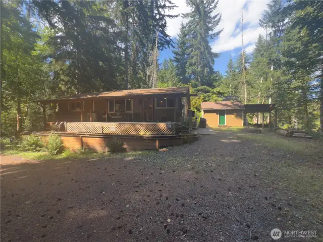 Large, covered wood storage next to large outbuilding.