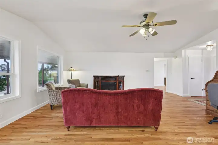 Living room with freestanding electric fireplace, large windows and oak hardwood floors.