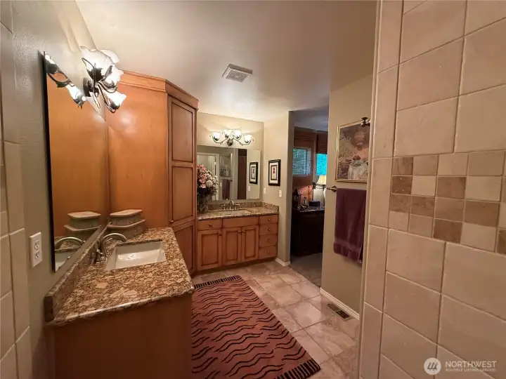 Another view of primary suite bathroom with spacious cabinetry and two separate granite vanities.