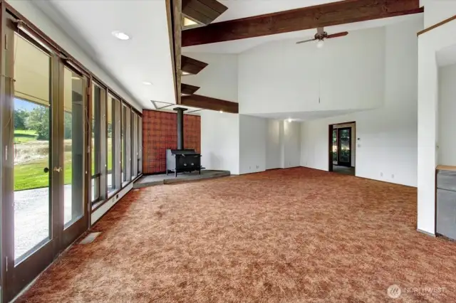 An alternative view of the vaulted great room, featuring French doors on the left, along with the period-tiled wall and a wood-burning fireplace with its hearth.