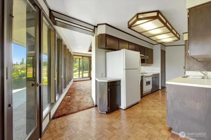A perspective from the eating space with the pantry located behind. An exterior door is positioned on the left along a continuous wall of floor to ceiling windows.