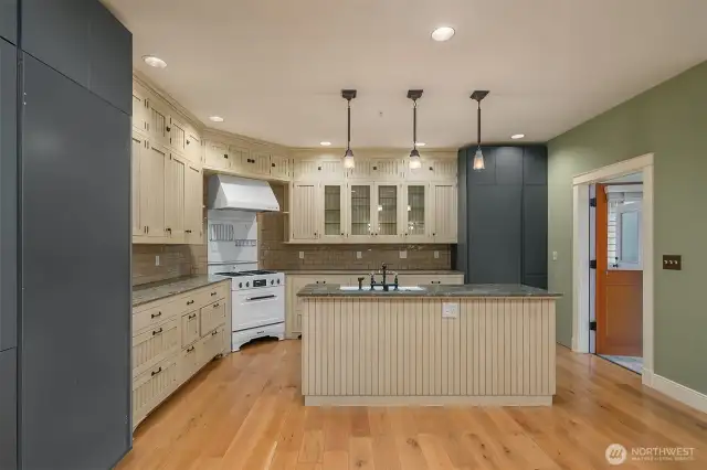 Kitchen has custom inset cabinets with scalloped half door, integrated appliances, slab granite counters, tile backsplash, under and interior cabinet lighting, farm sink and bridge mounted faucet