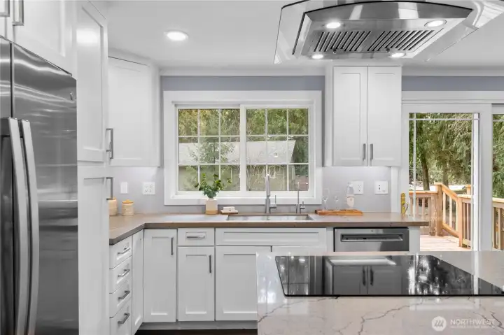 Suspended above the island, the modern stainless steel hood becomes a striking architectural feature with its graceful curved form and clean lines. Its brushed steel finish coordinates beautifully with the surrounding appliances, and integrated lights beneath it cast a soft glow over the cooktop. The sleek glass cooktop below offers a smooth surface that’s easy to maintain, helping the kitchen stay effortlessly polished.  Weekend breakfasts take shape here with ease, and an elegant dinner comes together just as naturally, all while loved ones sit comfortably at the breakfast bar across the island. Quartz counters extend around the cooking space, offering generous room for ingredients and serving pieces while keeping conversation close and uninterrupted.