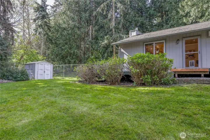 Rear exterior of the home set with one shed, additional wood storage is around the corner