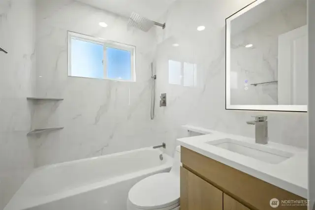 Beautiful large panel tiles on every wall are softened by a warm wood tone vanity w/ a a quartz countertop.