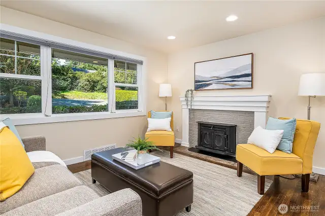 The front living room welcomes you as you enter, filled with natural light from two skylights and large windows that offer serene views of the front yard. A fireplace with insert adds warmth and comfort for cozy winter days.