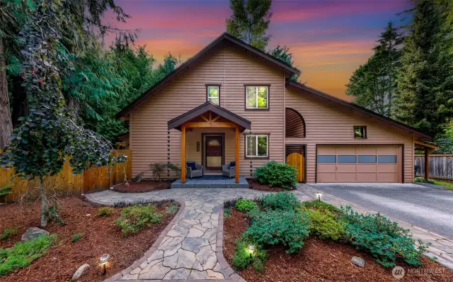 At twilight, the front of the home glows against a vibrant sky, with uplighting illuminating the landscaped entry and charming covered porch. A stunning introduction to this private Geneva retreat.