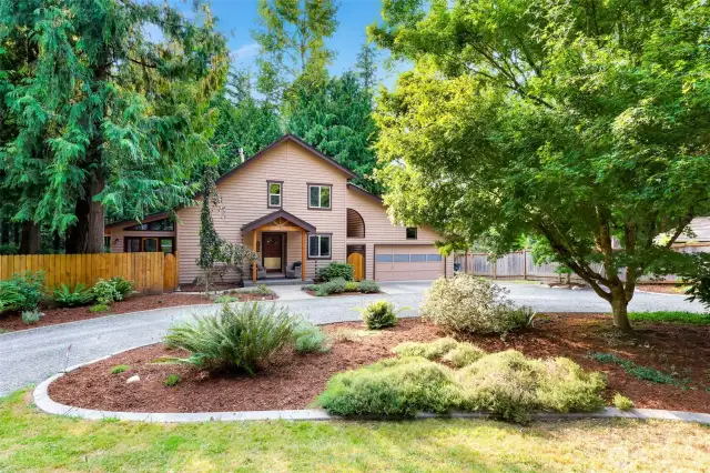 Framed by tall trees and fresh landscaping, the home’s front profile showcases Northwest charm with its wood siding, dual garage, and inviting covered entry.