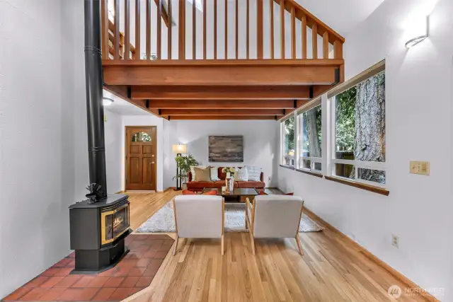 From beneath the mezzanine, this view captures the true essence of the home: nature outside every window, warmth at the hearth, and a layout designed for connection.