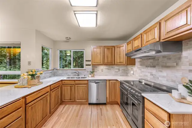This polished chef’s kitchen showcases a luxury gas range, sleek quartz countertops, and full-height tile backsplash. Oversized windows fill the space with light and nature.