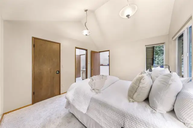 The spacious primary bedroom offers elevated privacy with access to both bathrooms and the sunroom loft. Vaulted ceilings, dual closets, and peaceful outdoor views complete the retreat.