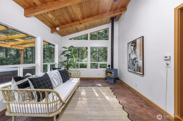 A second angle of the sunroom reveals its connection to the outdoor deck and the home’s natural setting. Floor-to-ceiling windows bring the outside in, while the wood-paneled ceiling adds warmth overhead.