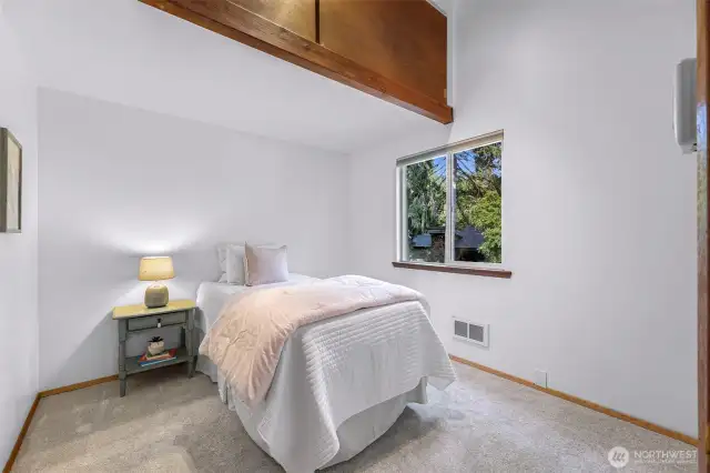One of the upstairs bedrooms offers a peaceful retreat with treetop views, soft carpet underfoot, and space for restful slumber or creative pursuits.