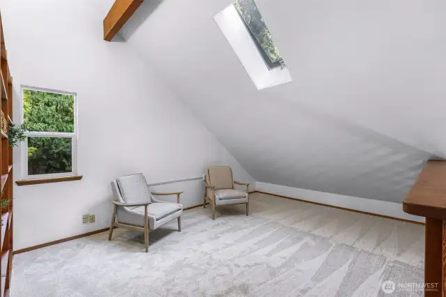 Bathed in natural light from the skylight and side window, this cozy loft space offers a serene escape under vaulted ceilings and exposed wood beams. With plush carpeting and a quiet ambiance, it’s ideal for reading, reflection, or a peaceful home office.