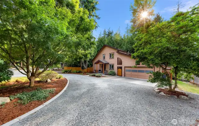 Framed by vibrant landscaping and lush trees, the welcoming front approach is both charming and functional. The gravel drive and landscaped walkway lead to a custom wood-accented entry.