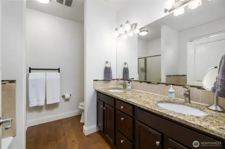 Double vanity with granite countertops in five piece primary ensuite bathroom.