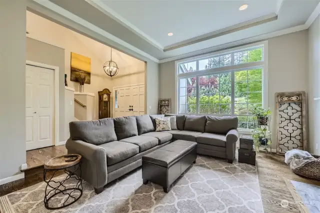 The living room features newer hardwood floors, dramatic panned ceilings and floor-to-ceiling picture windows overlooking the manicured and verdant front yard.