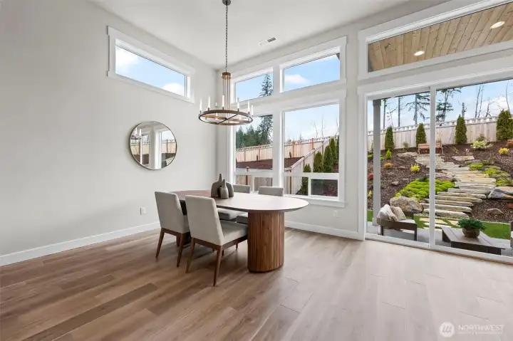 Dining area framed by a dramatic wall of windows overlooking the beautifully landscaped backyard, filling the space with natural light and showcasing indoor-outdoor living in this upgraded newer construction home in McCormick Trails, Port Orchard.