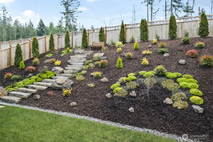Beautifully landscaped backyard featuring paving stone hardscape and curated seasonal color, creating an easy-maintenance outdoor sanctuary that enhances the upgraded newer construction lifestyle in McCormick Trails, Port Orchard.