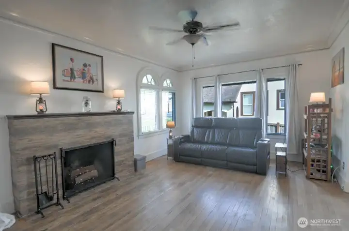 Spacious living room filled with natural light, featuring hardwood floors, charming arched windows, and a cozy fireplace that adds warmth and character to the space.