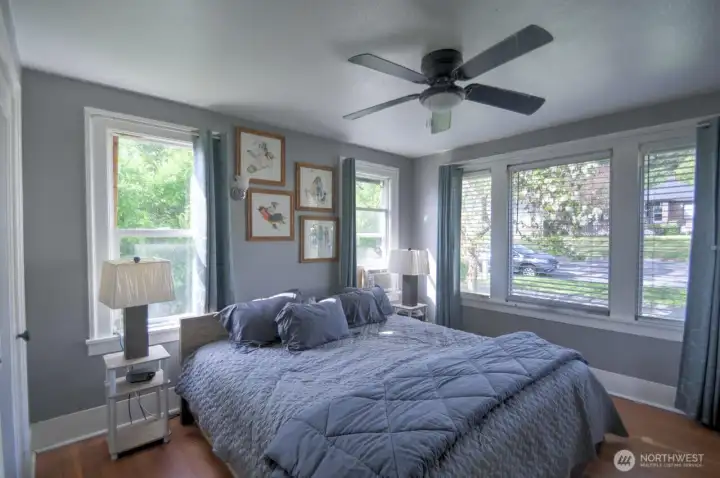 Spacious main floor primary bedroom filled with natural light, featuring large windows, hardwood floors, and a comfortable, relaxing atmosphere.