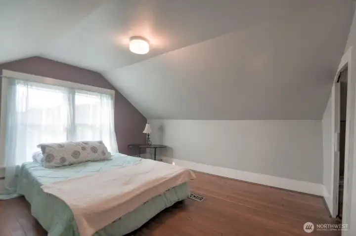 Spacious upstairs bedroom featuring hardwood floors, charming vaulted ceilings, and a cozy atmosphere with plenty of natural light.