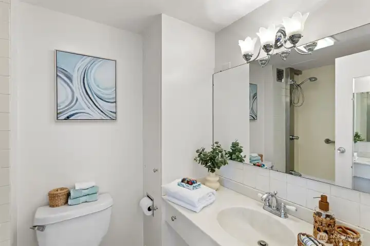 The bathroom is clean and bright, with a long vanity, generous mirror, and a classic tiled shower surround.