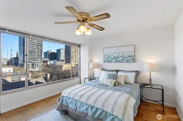 The bedroom keeps the same bright, open feel with expansive windows, a generous mirrored closet that amplifies the space, and a window A/C unit for warm days.