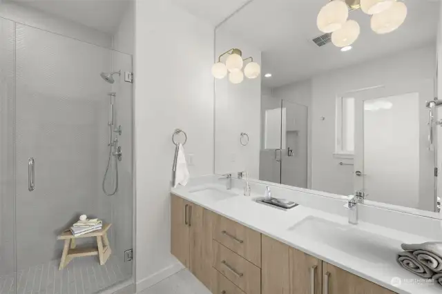 The pristine primary bath features dual-sink vanity, spacious rain shower & under cab lighting. This photo is virtually staged.