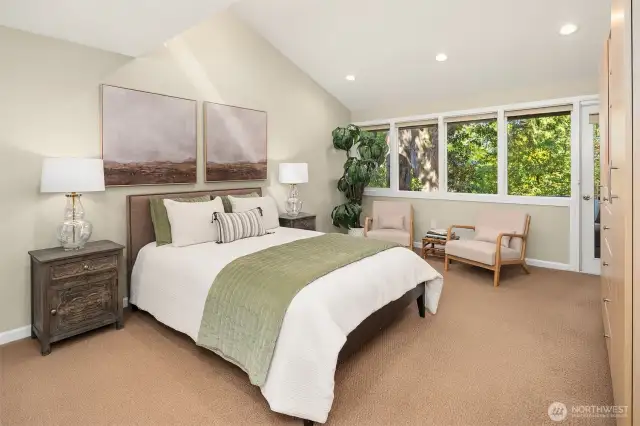 Luxurious primary bedroom featuring vaulted ceiling, wall of windows and door to private deck,