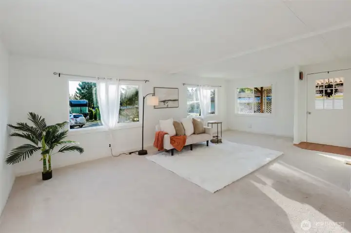 Comfortable living room anchored by large windows, creating a light-filled environment with views of the surrounding greenery.