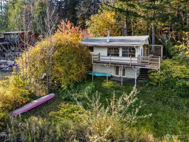 Aerial view of cabin with main level and unfinished basement from the lake side. Mature trees and plantings.