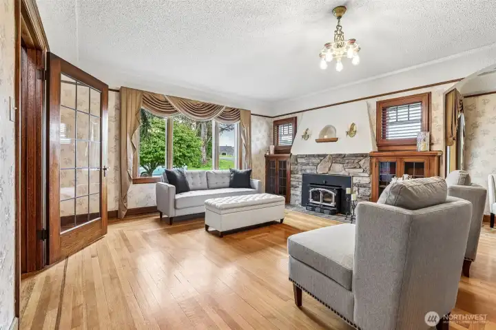 This living room has old world charm with modern updates. Charming stone fireplace, built-in glass front cabinets, wood wrapped windows & original hardwood floors with custom inlays.
