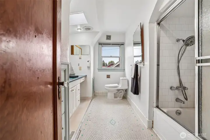 Hall bathroom with penny tile flooring, tub/shower, laundry chute, skylight , built-in storage & large vanity.