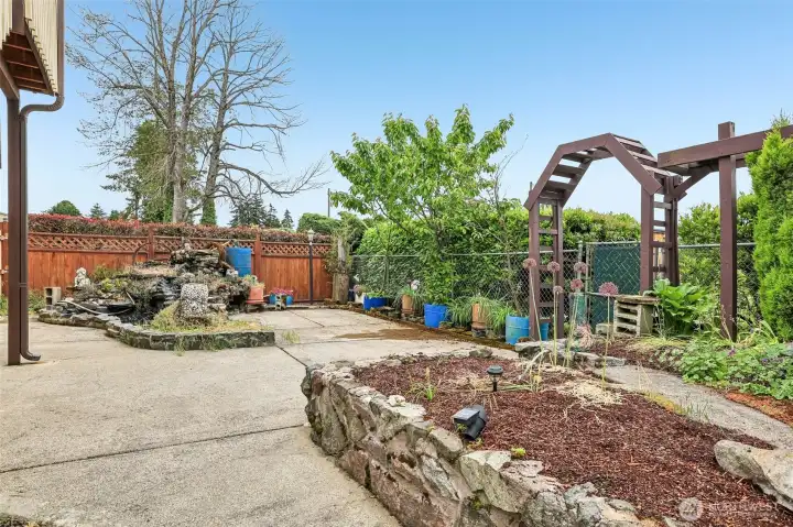 Large patio with water feature with waterfall, planting beds & another water feature out of the photo