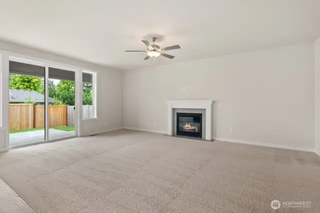 Large living room with gas fireplace, oversized windows, ceiling fan and slider door that opens to backyard.