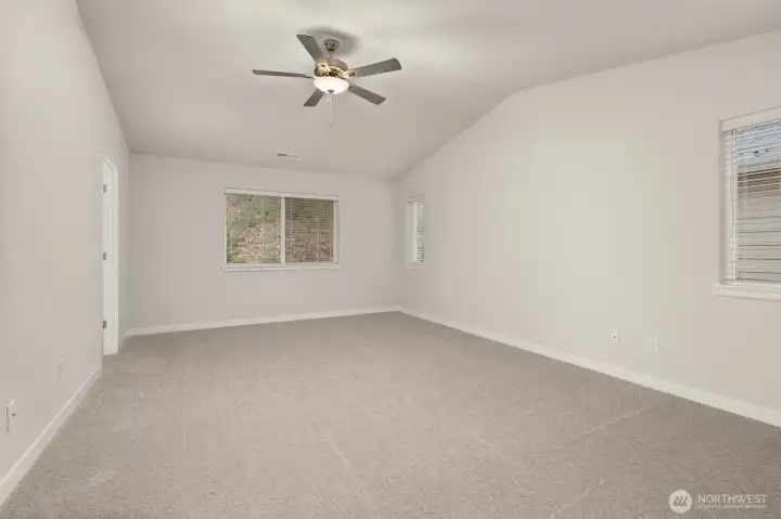 Spacious primary bedroom features vaulted ceilings, large windows for natural light, and a ceiling fan for added comfort.