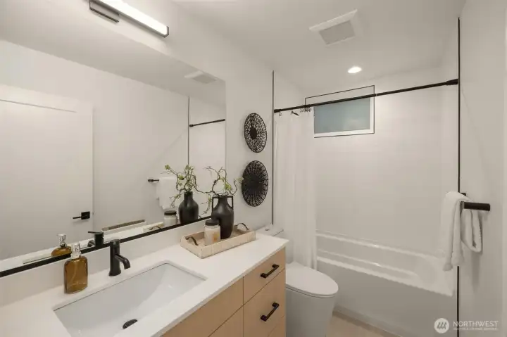 Contemporary bathroom complete with a modern vanity, large mirror, and clean tub-to-ceiling tile surround. (photos are of model home, similar finishes & quality)