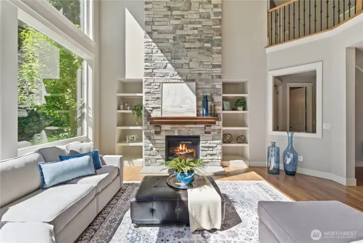 A warm, inviting family room with built-ins around the gas fireplace, a peek at the second floor, and windows fitted with electric exterior shades to soften the afternoon light