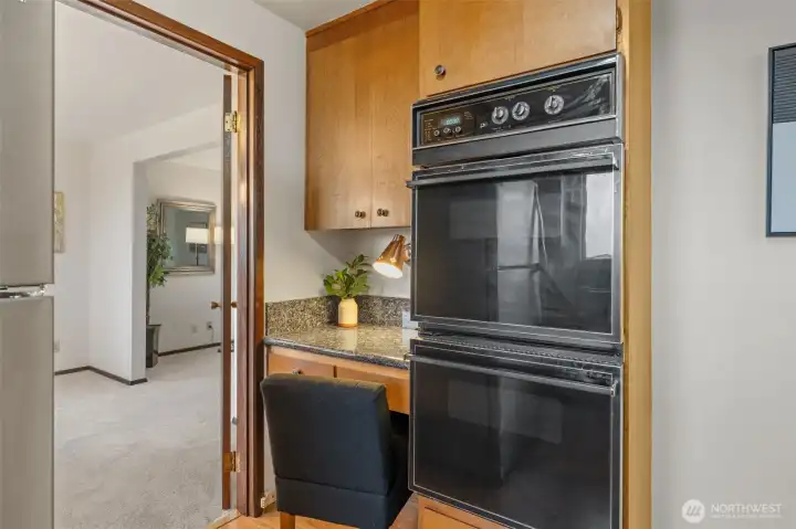 Double ovens offer added cooking capacity, ideal for gatherings and holiday meals. A built-in workspace nearby provides a spot for planning recipes or keeping the chef company.